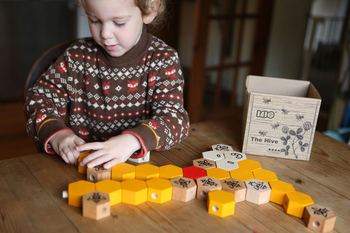 Child playing with the Bajo plastic-free stacking wooden hive blocks on a wooden table