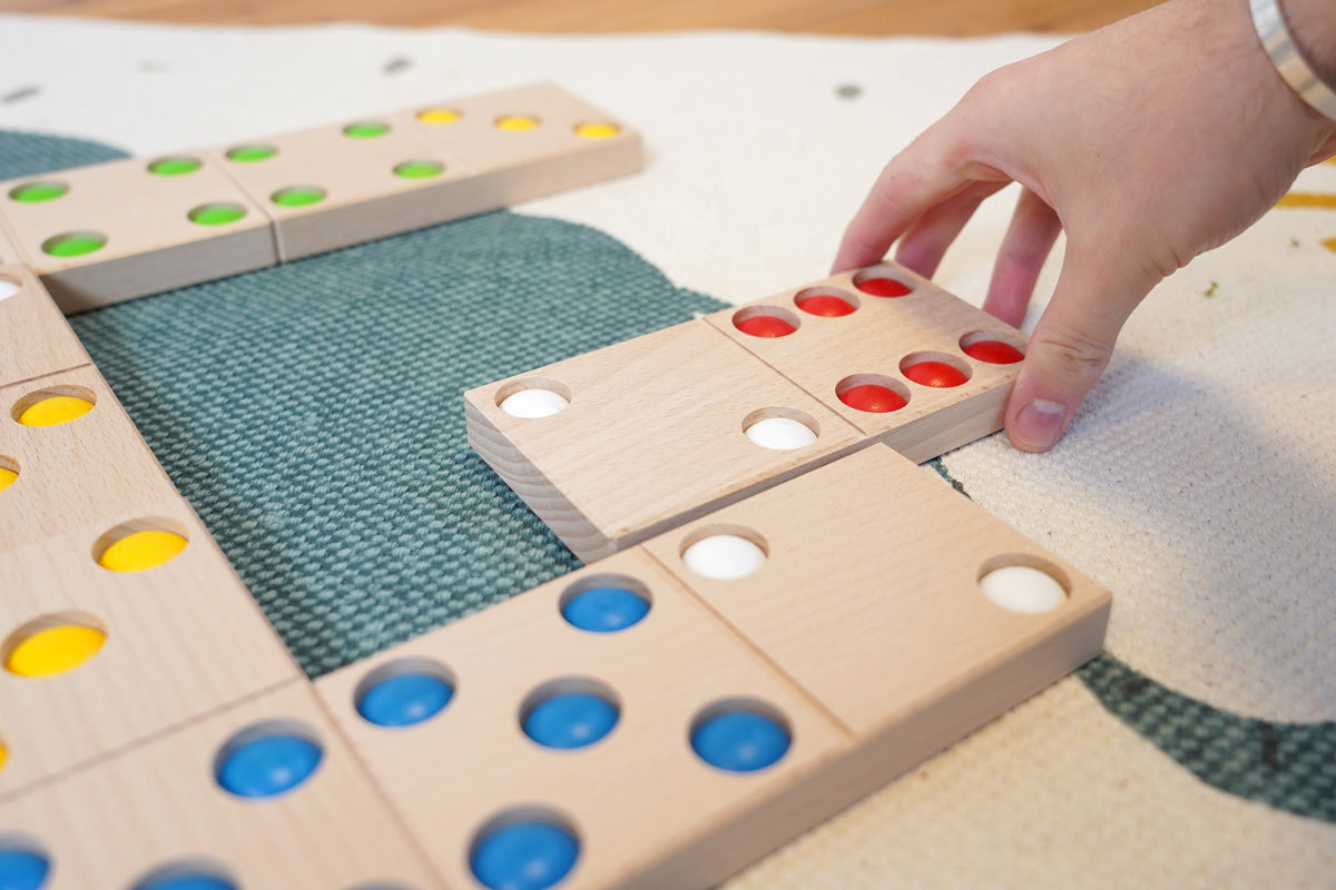 Close up of a hand moving the Bajo XXL wooden dominos on a blue and white carpet