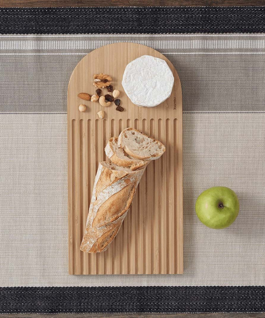 A Bambu bamboo Arch Bread Board with a baguette, cheese and nuts on it. 