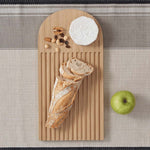 A Bambu bamboo Arch Bread Board with a baguette, cheese and nuts on it. 