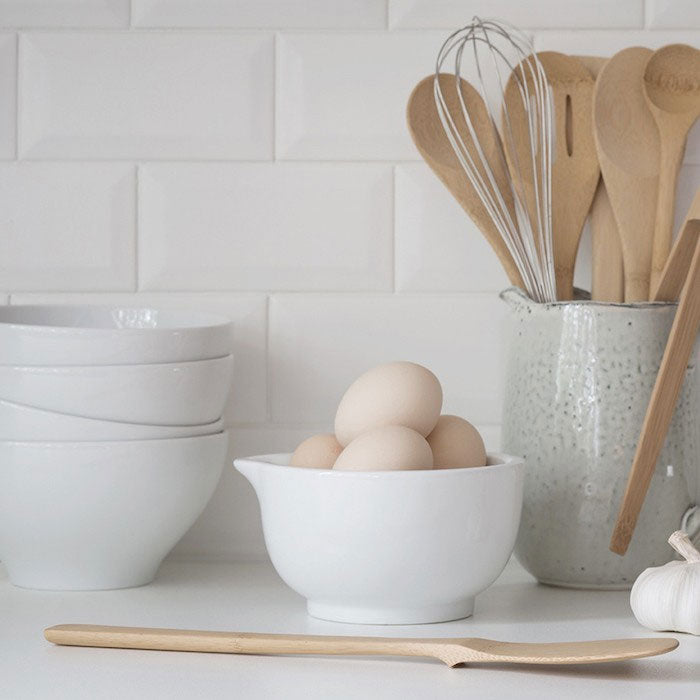 Bambu Give It A Rest Bamboo Spatula placed on kitchen counter with a bowl of eggs and pot of wooden utensils behind