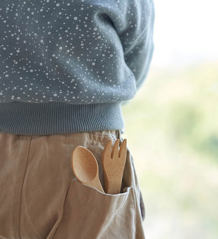 The Bambu Bamboo kids fork and spoon shown pepping out of a child's back pocket.