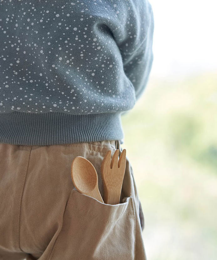 The Bambu Bamboo kids fork and spoon shown pepping out of a child's back pocket.