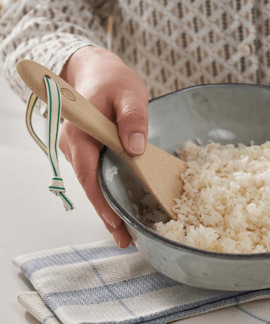 A Bambu Bamboo Rice Paddle in a bowl of rice being held by a person. 