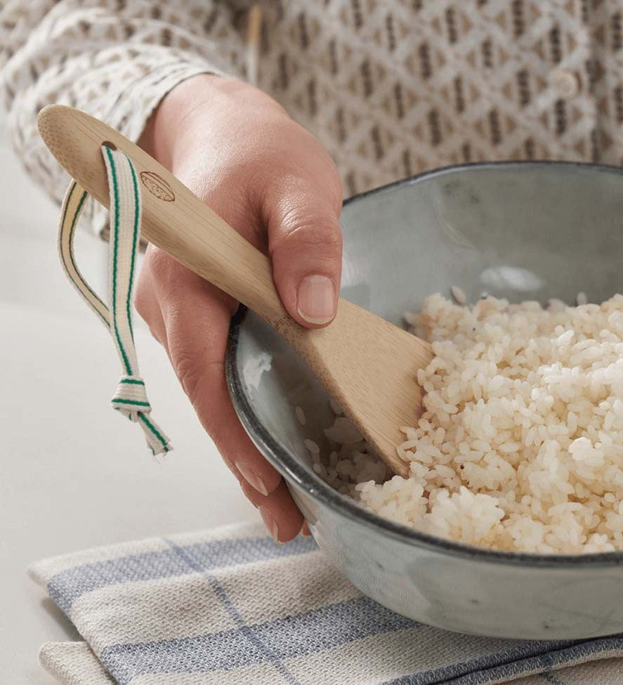 A Bambu Bamboo Rice Paddle in a bowl of rice being held by a person. 