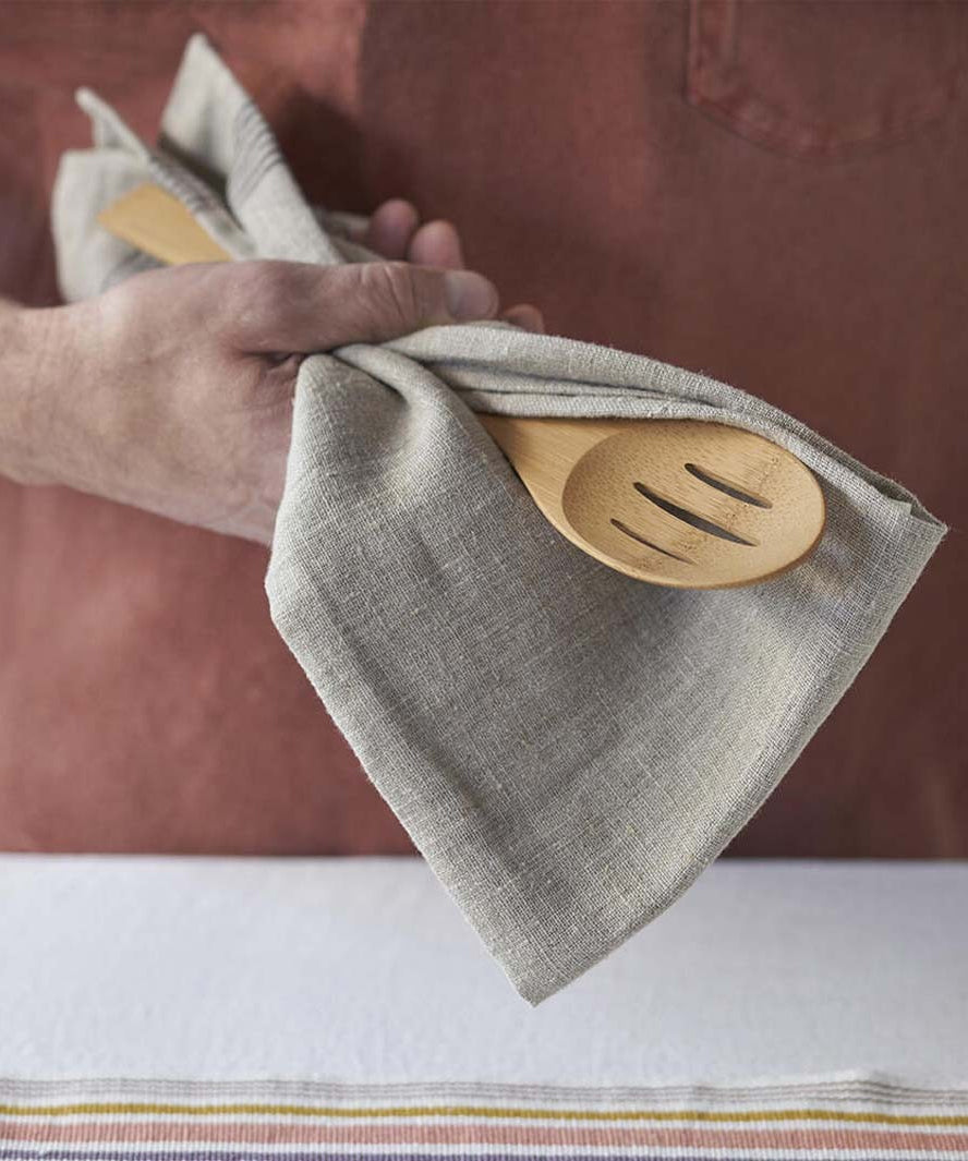 A close up of a person holding a Bambu Bamboo Give It A Rest Slotted Spoon with a linen cloth in their hand.  