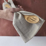 A close up of a person holding a Bambu Bamboo Give It A Rest Slotted Spoon with a linen cloth in their hand.  