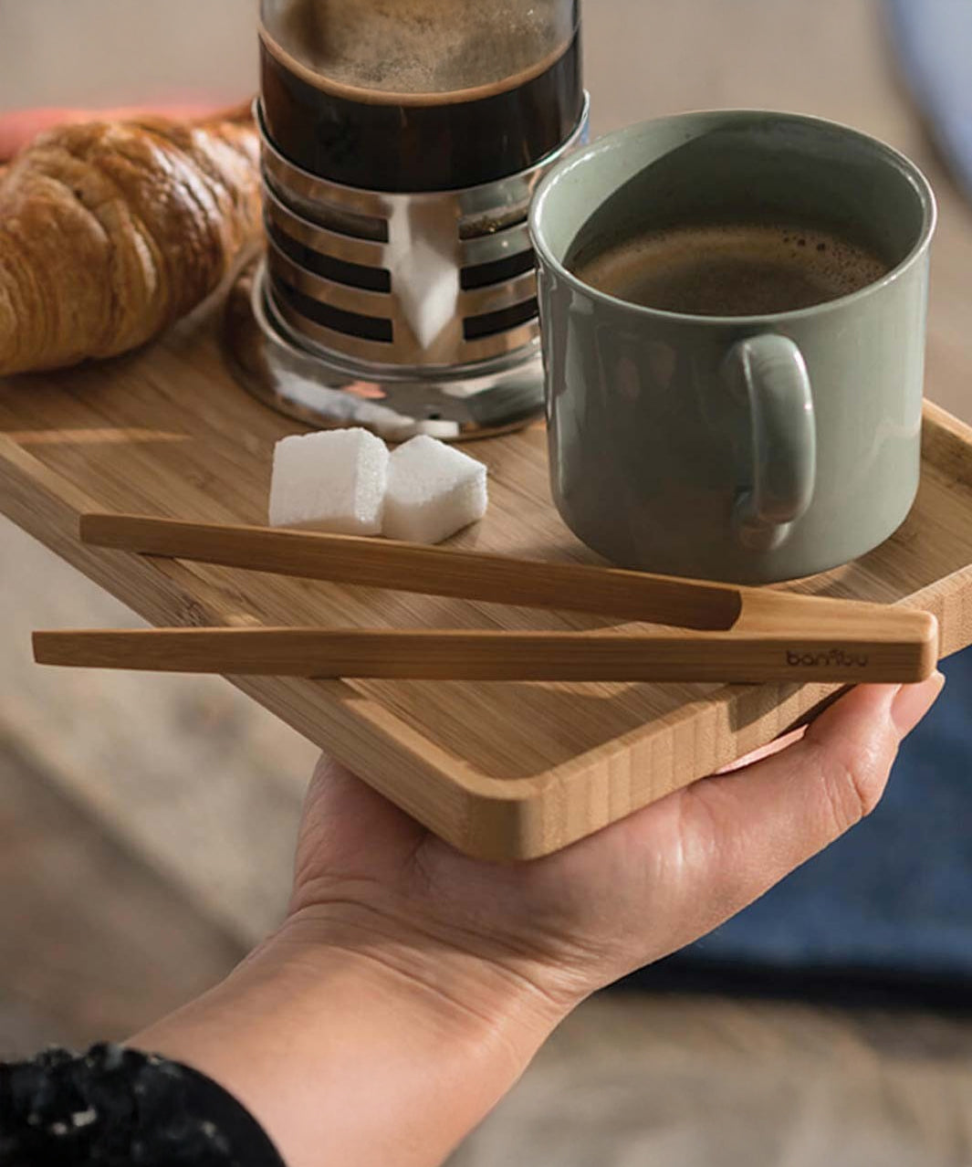 The Bambu Tiny Tongs shown on a wooden tray alongside coffee cups and a croissant. 