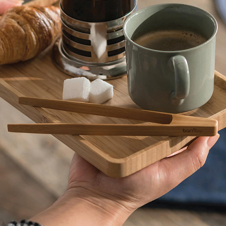 tiny tongs placed on a try next to a cup of coffee and some sugar cubes