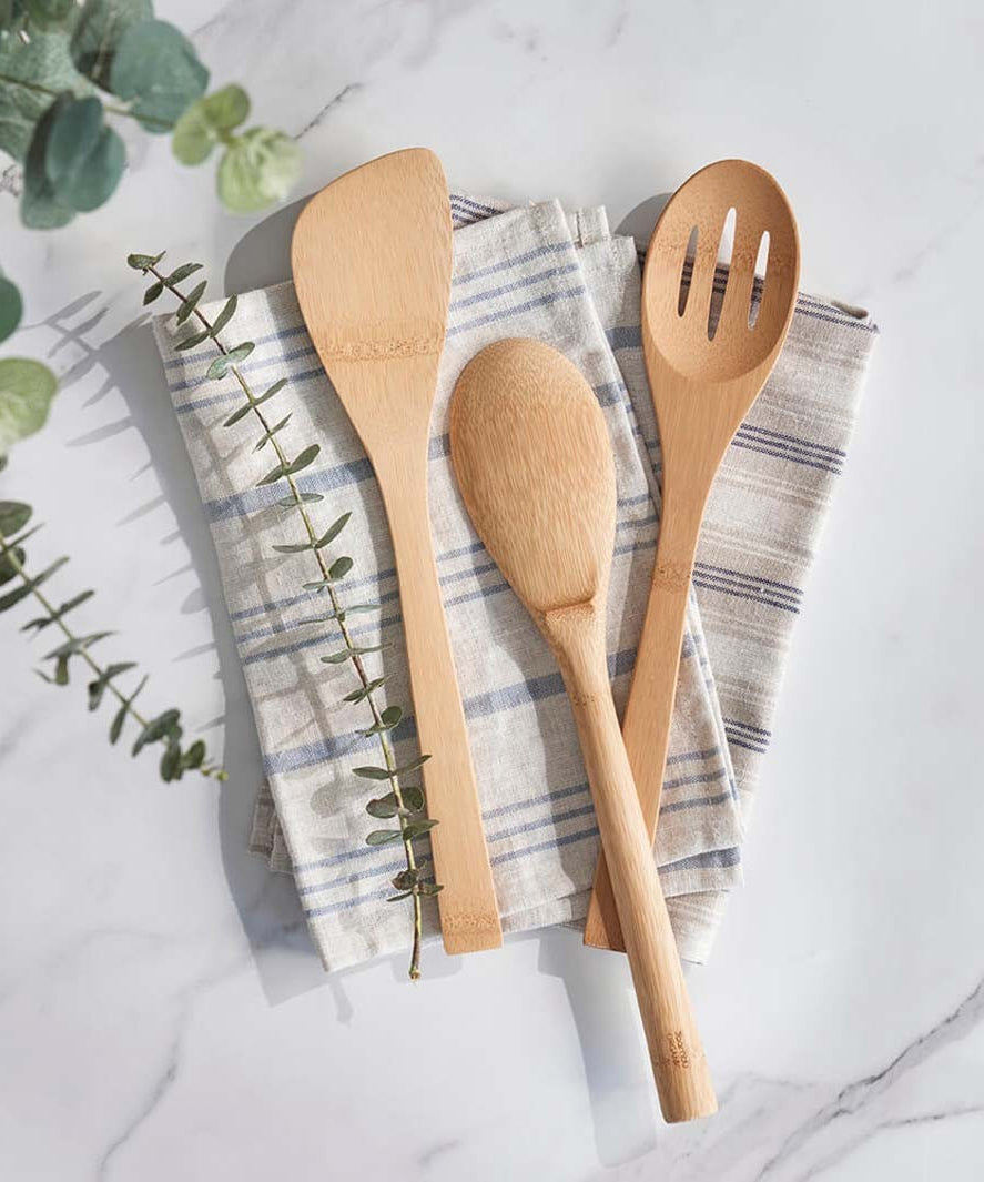 Three utensils from the Bambu Give It a Rest bamboo utensils range placed on folded tea towels on a marble surface. 