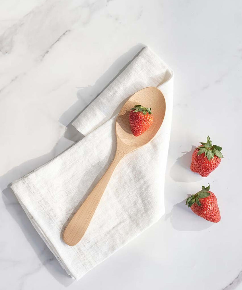 A Bambu Serving Spoon placed on a white linen cloth with a strawberry on it. 