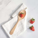 A Bambu Serving Spoon placed on a white linen cloth with a strawberry on it. 