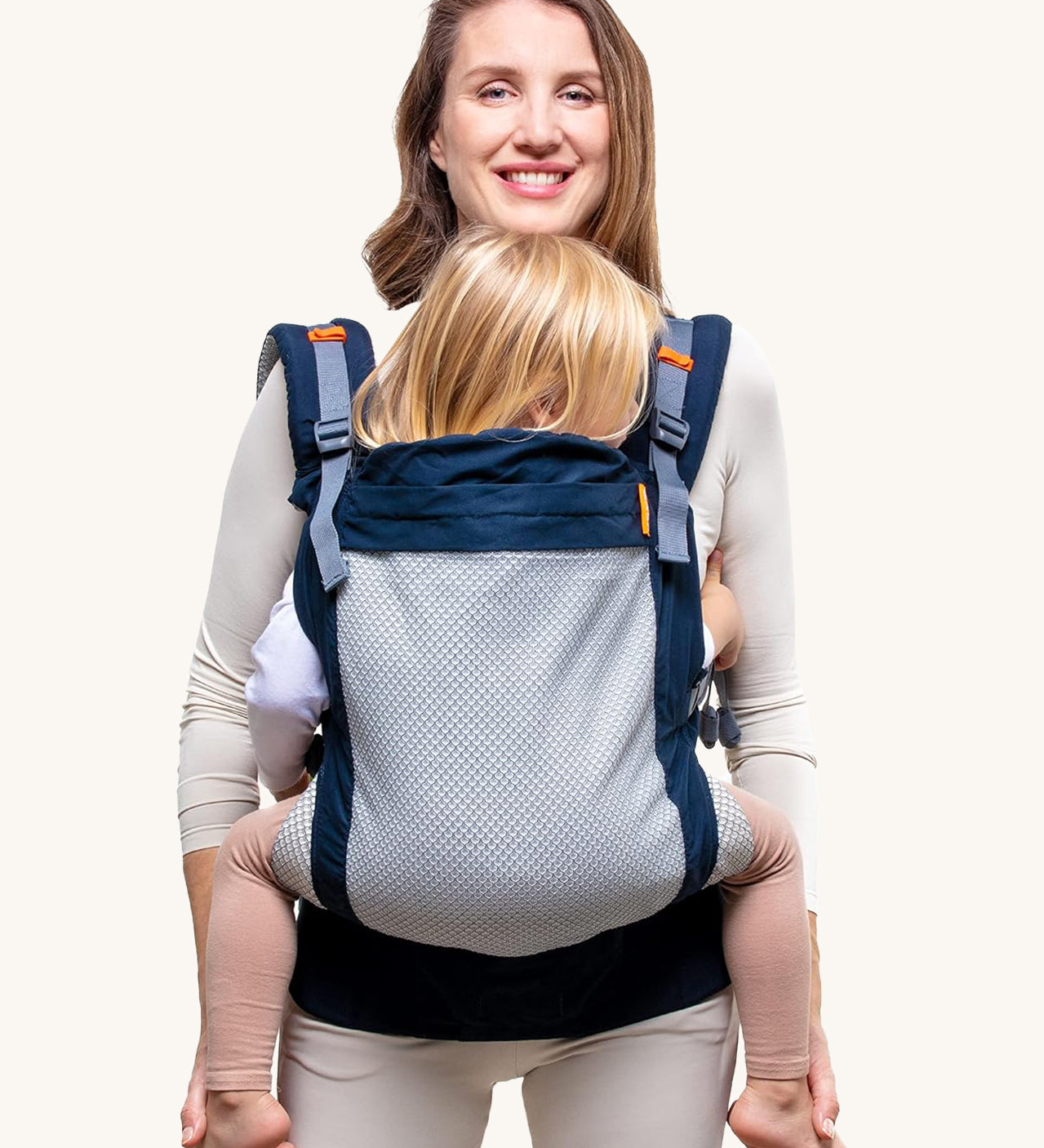 Beco Toddler Carrier - 20-60lb. The image shows an adult earing the carrier with a toddler inside. The carrier is navy blue with a mesh back, and orange detail, on a cream background