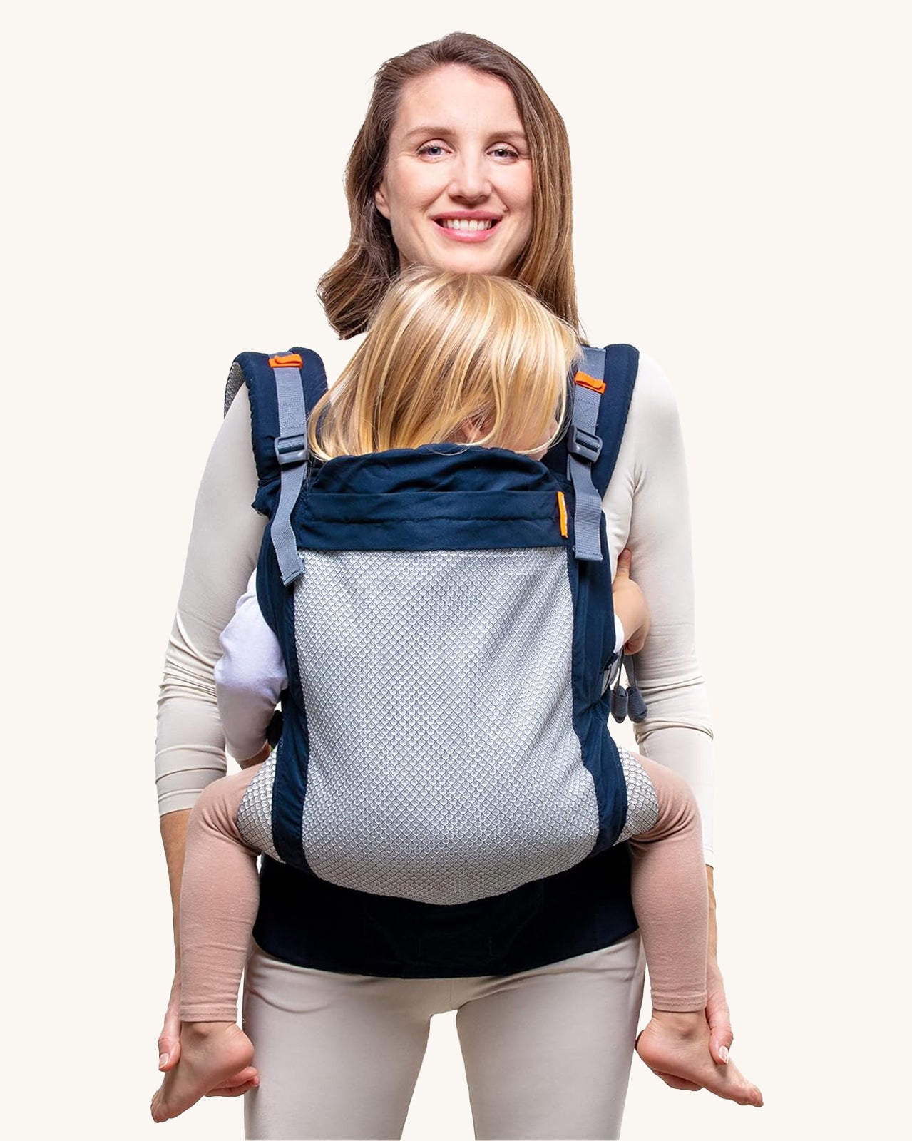 Beco Toddler Carrier - 20-60lb. The image shows an adult earing the carrier with a toddler inside. The carrier is navy blue with a mesh back, and orange detail, on a cream background