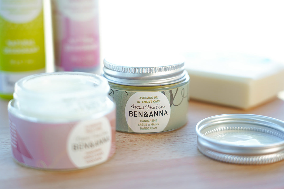 Close up of Ben & Anna eco-friendly natural oil hand moisturising creams on a wooden worktop next to some Ben & Anna roll on deodorant and soap