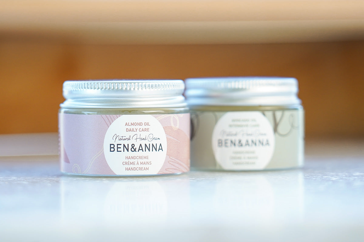 Close up of Ben & Anna sustainable natural oil hand creams on a white marble floor in front of a wooden background