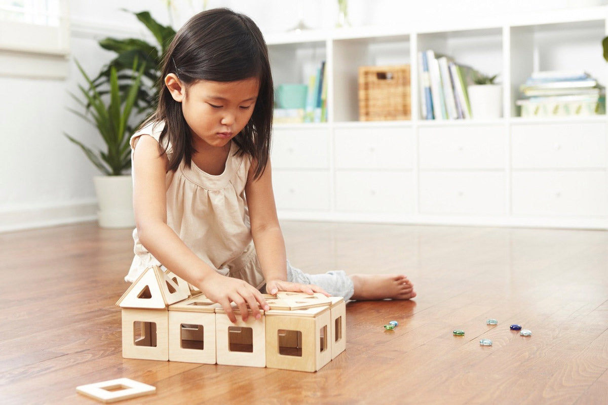 Girl playing with a set of Big Future Wooden Earth Tiles on a wooden floor in a white living room