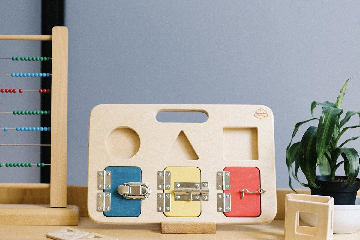 Big Future Toys wooden latch board on its stand on a wooden table next to an abacus in front of a grey wall