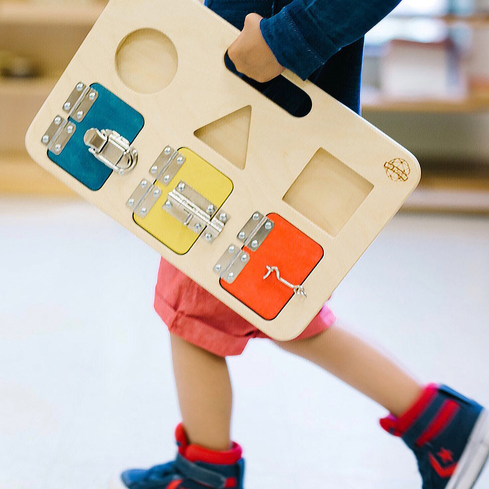 Child in red shorts walking on a white floor carrying the Big Future Toys Latch Board