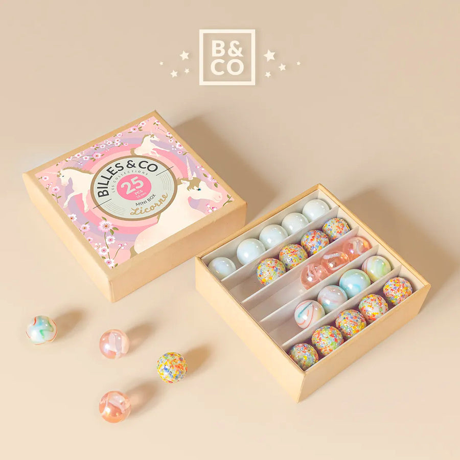 Billes & Co rainbow unicorn glass marbles set open on a beige background with some colourful marbles scattered next to the box