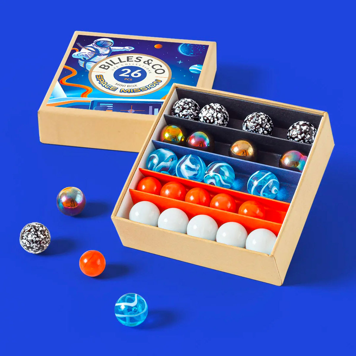 Billes & Co kids recycled glass space mission mini marbles set open on a blue background with some coloured marbles scattered around the box