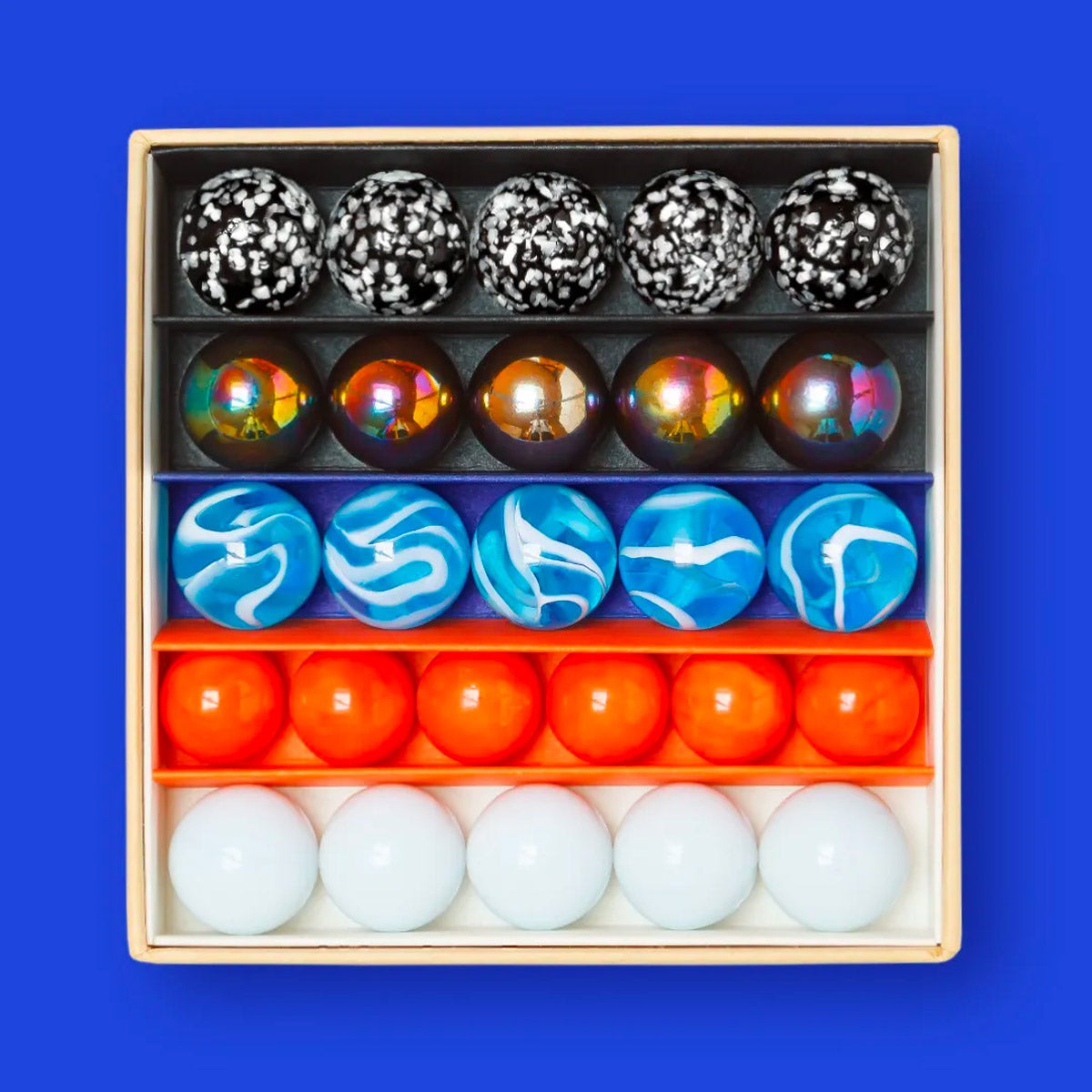 Close up of the Billes & Co colourful mini glass space mission marbles in their box on a blue background