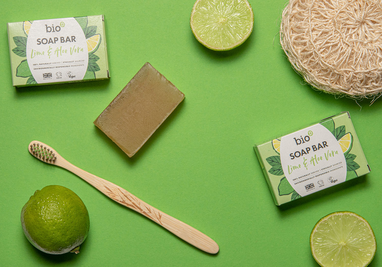 Bio-D natural Vegan aloe vera and lime soap bar on a green background surrounded by limes and a bamboo toothbrush