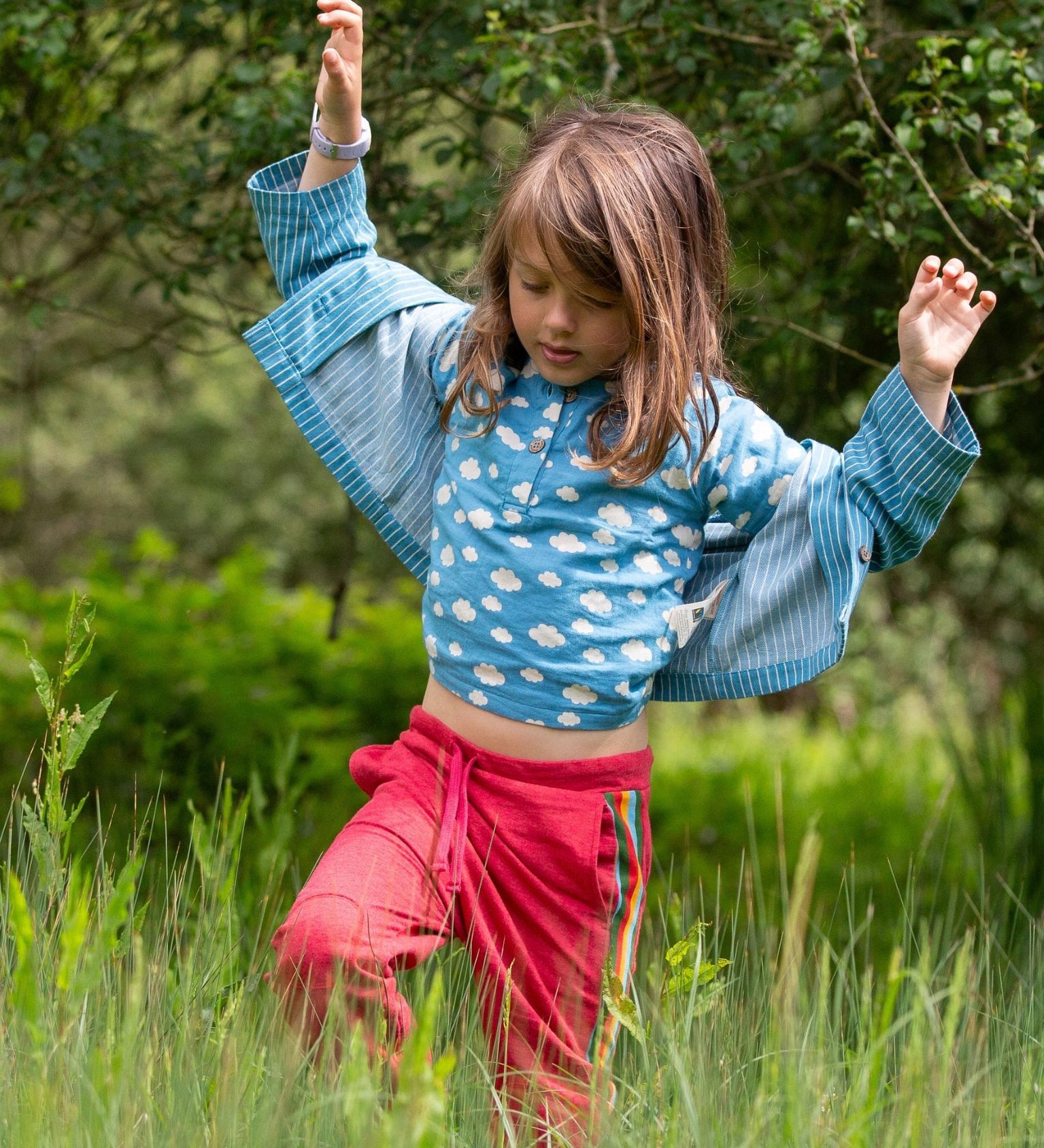 A child wearing the Little Green Radicals Kids Organic Cotton Blue Clouds Loose Fit Short Sleeve Henley Top with a striped blue shirt on top. 