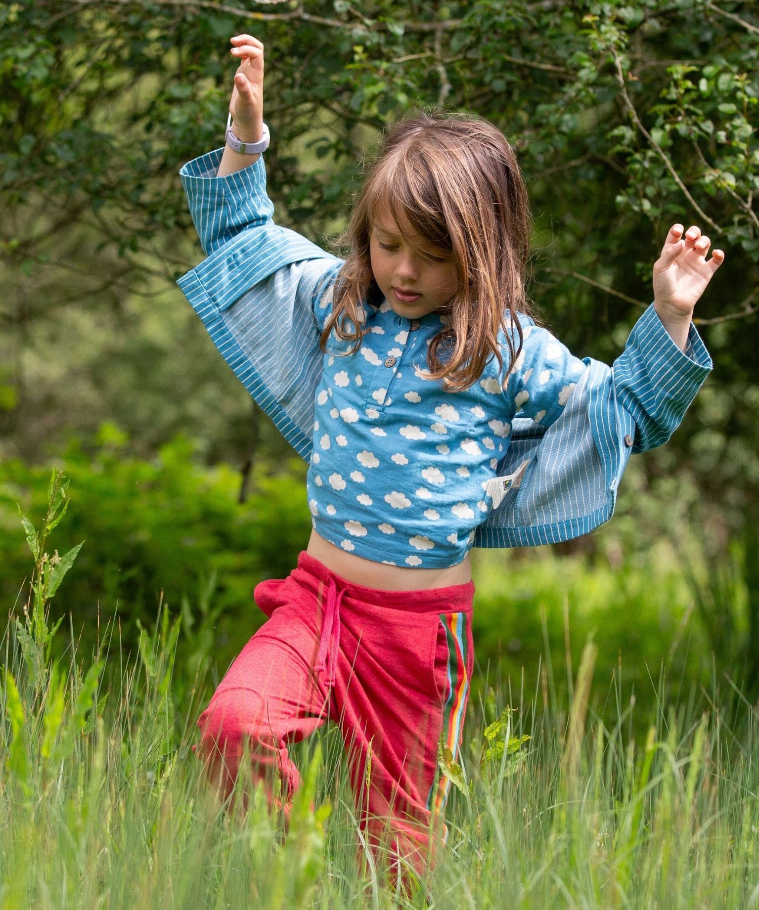 A child wearing the Little Green Radicals Kids Organic Cotton Blue Clouds Loose Fit Short Sleeve Henley Top with a striped blue shirt on top. 