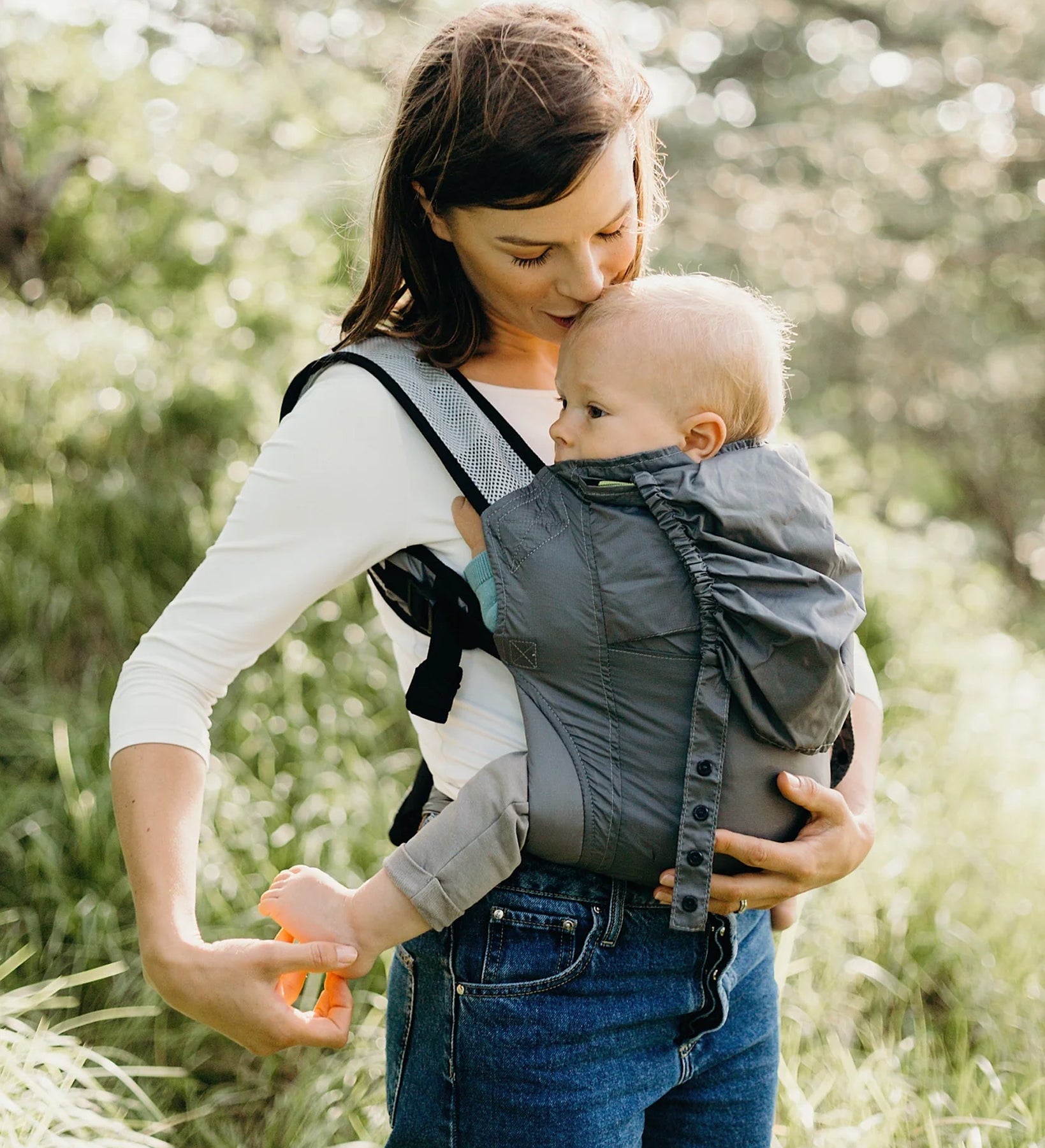 A parent outside in front of trees, carrying their child in the Boba Air Baby Carrier Ultra Lightweight - Grey