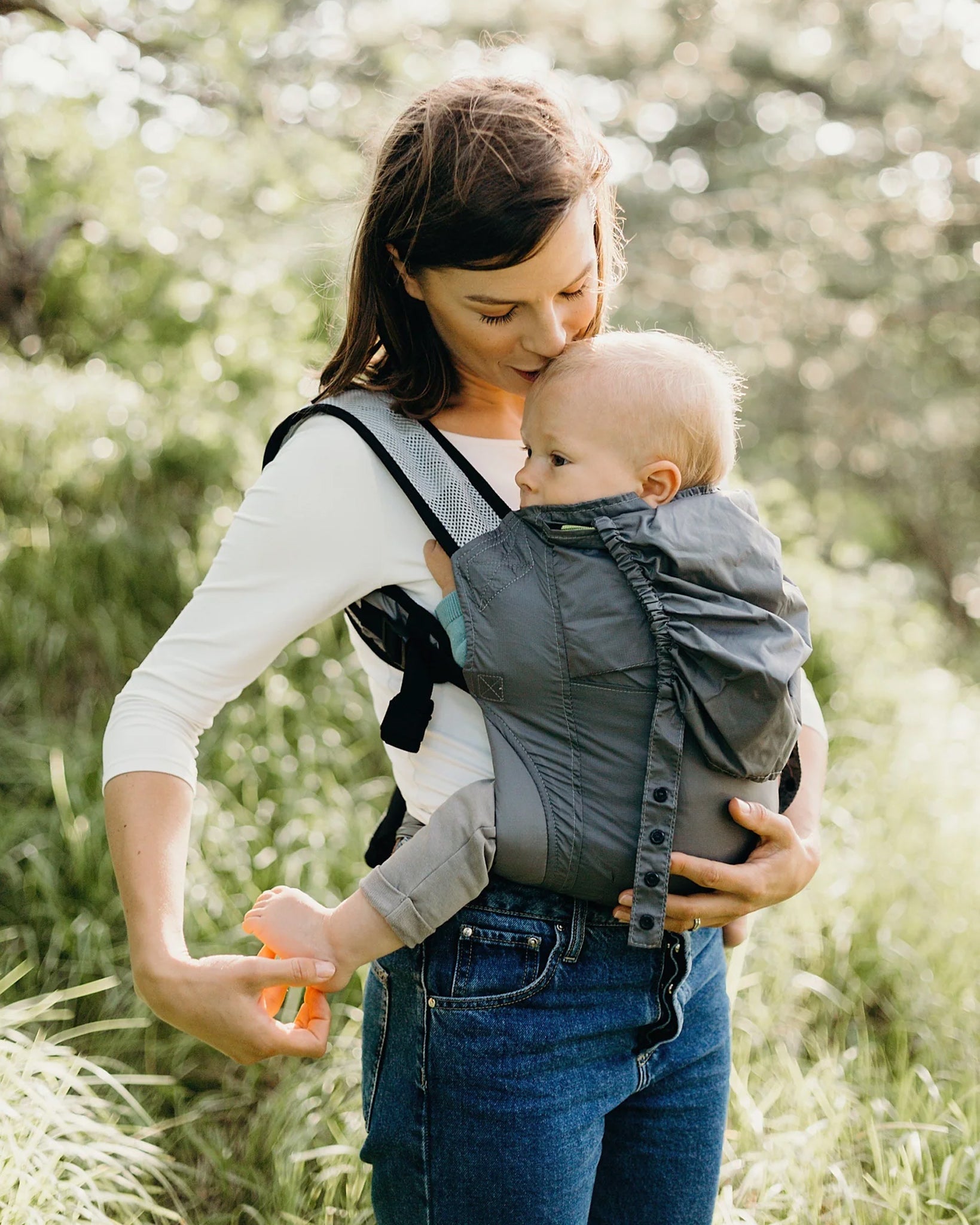 A parent outside in front of trees, carrying their child in the Boba Air Baby Carrier Ultra Lightweight - Grey