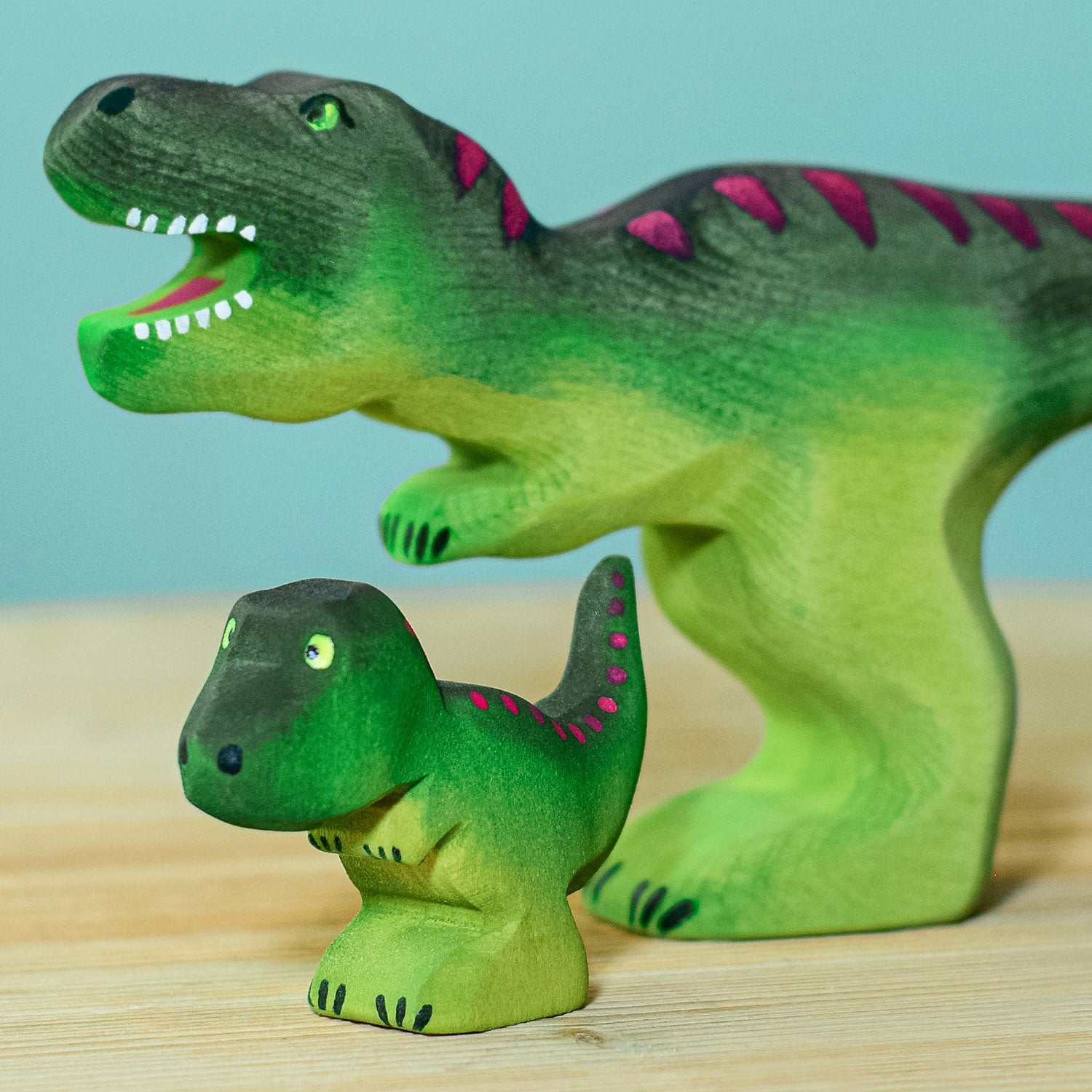 Wooden toy baby T-Rex in vibrant shades of green and purple. The baby T-Rex stands upright in a forward stance. The toy has painted eyes