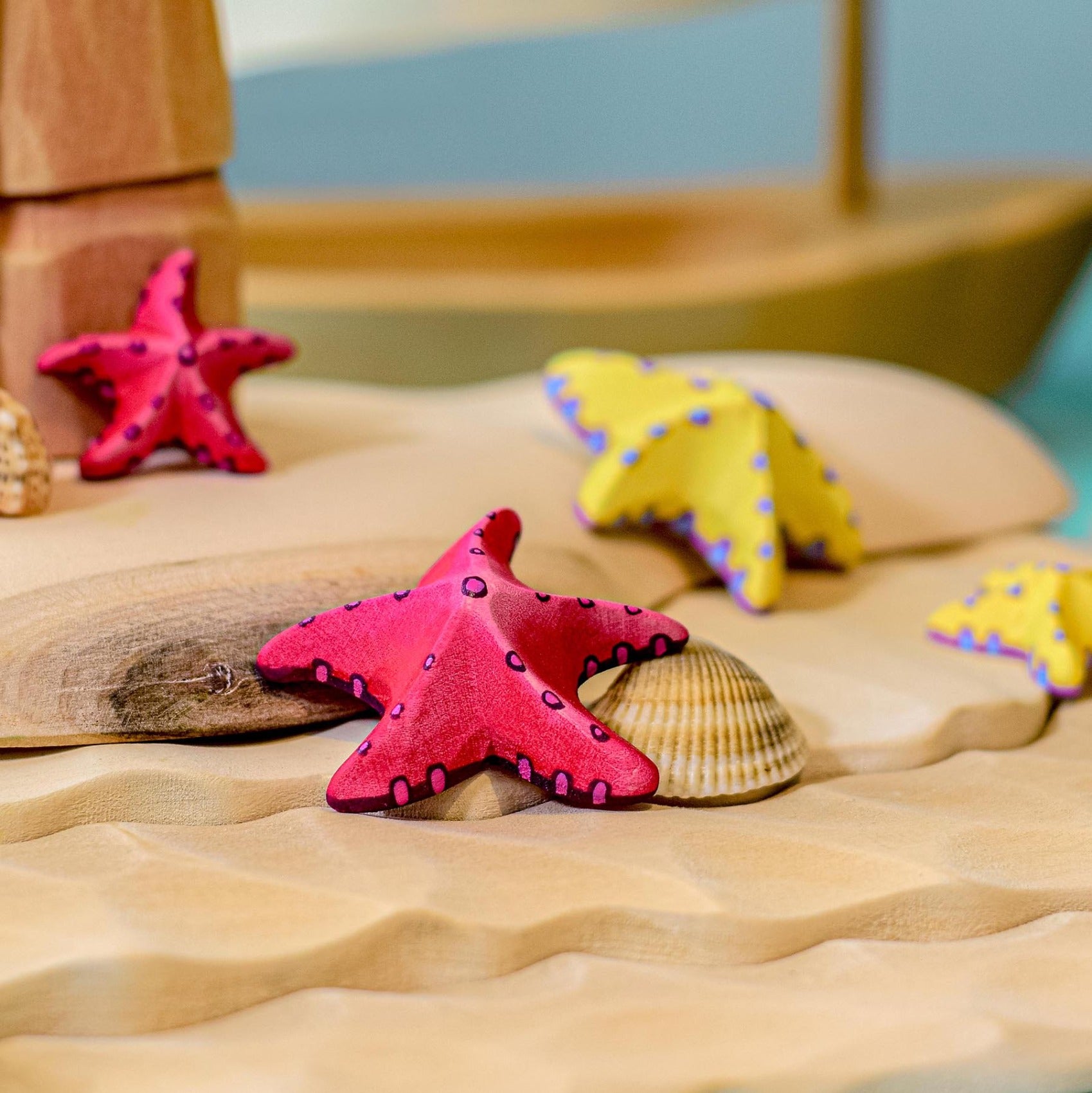 Bumbu Wooden Red Starfish Set posed next to a seashell.