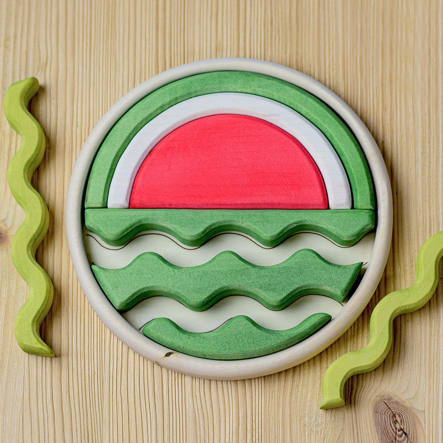 A round wooden puzzle depicting a watermelon. Different shapes fit together to create the final image