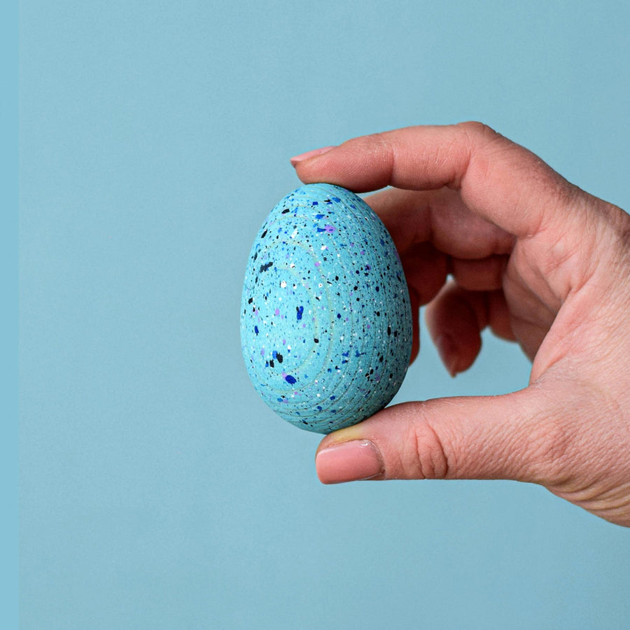 A speckled Blue Wooden Bumbu Brontosaurus Egg being held in a persons hand