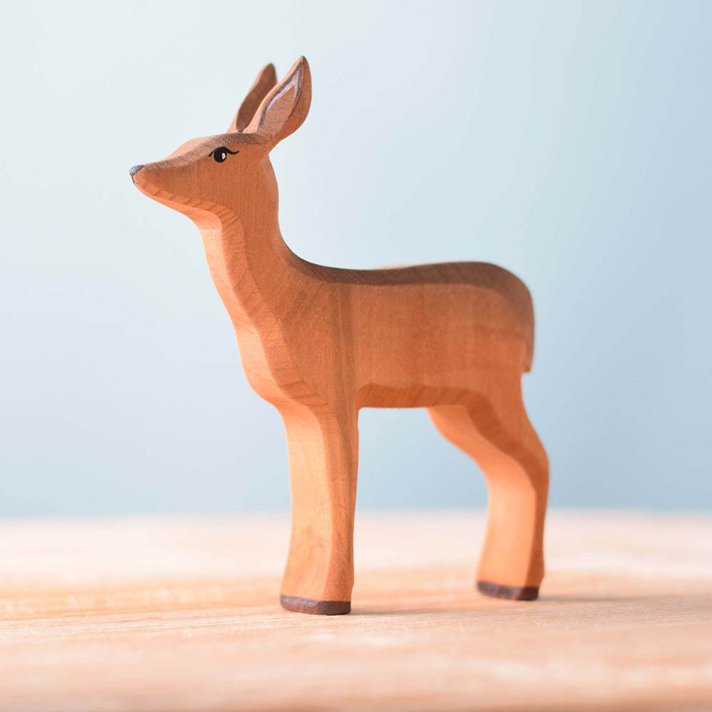 Close up of the Bumbu childrens wooden deer toy on a wooden worktop in front of a blue background