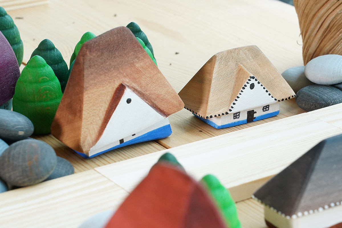 Close up of the Bumbu solid wooden Bucovina house toys on a wooden table next to some grapat mandala trees