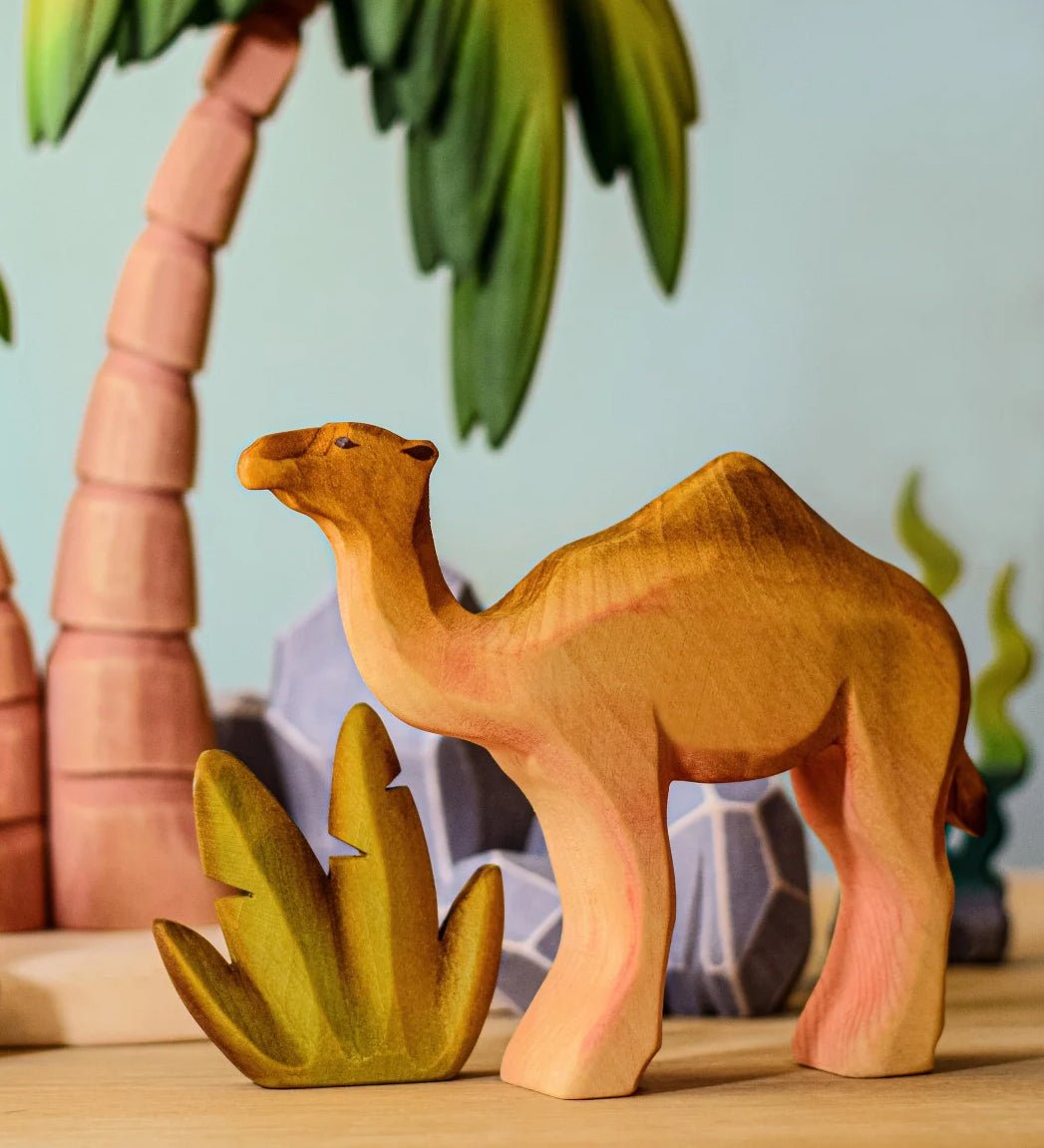 Bumbu handmade wooden camel figure standing in front of desert palm trees