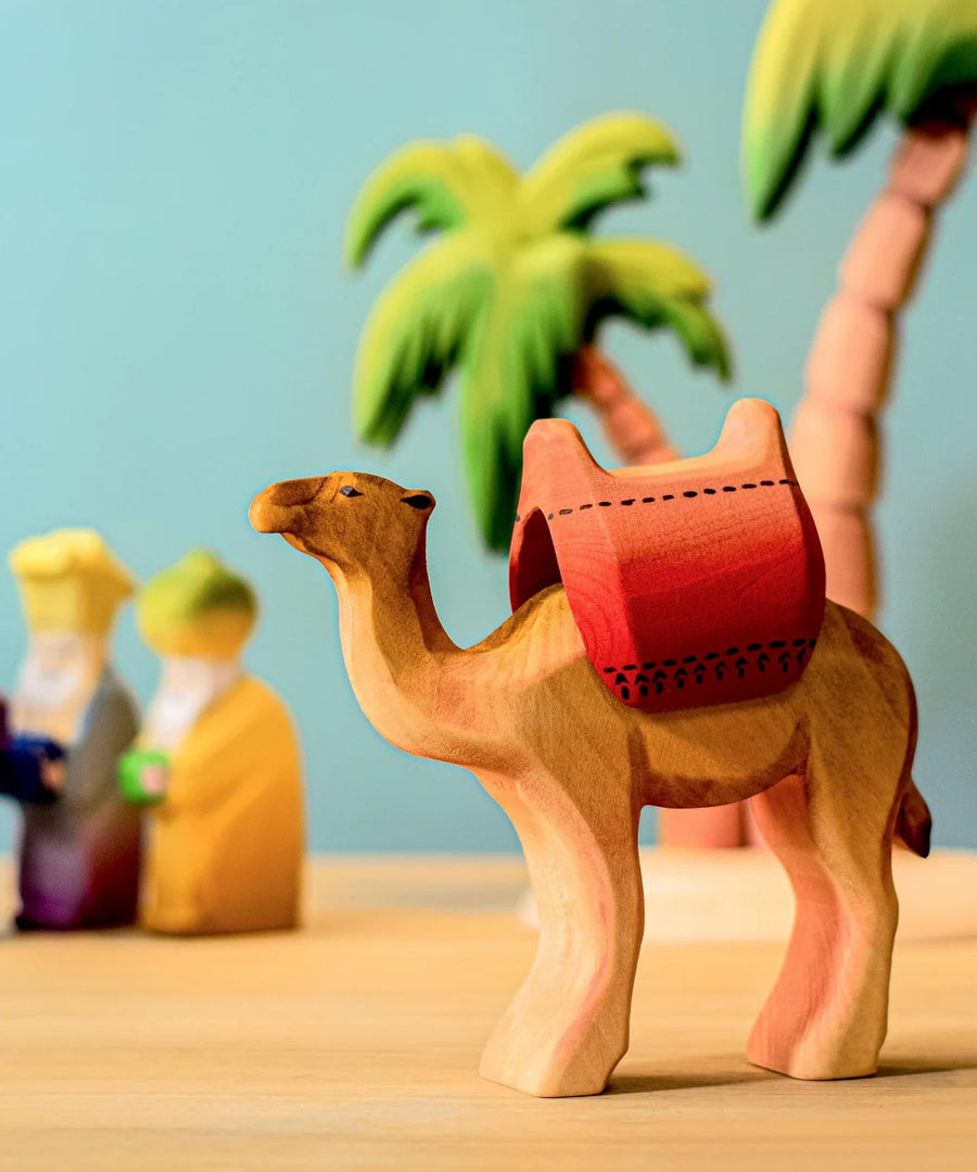 Bumbu wooden camel with red saddle pictured in a small world play scene with three kings and Bumbu palm trees in the background.