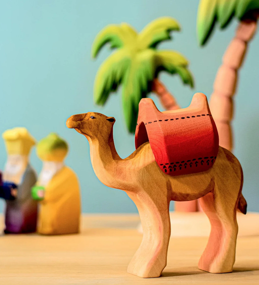 Bumbu wooden camel with red saddle pictured in a small world play scene with three kings and Bumbu palm trees in the background.