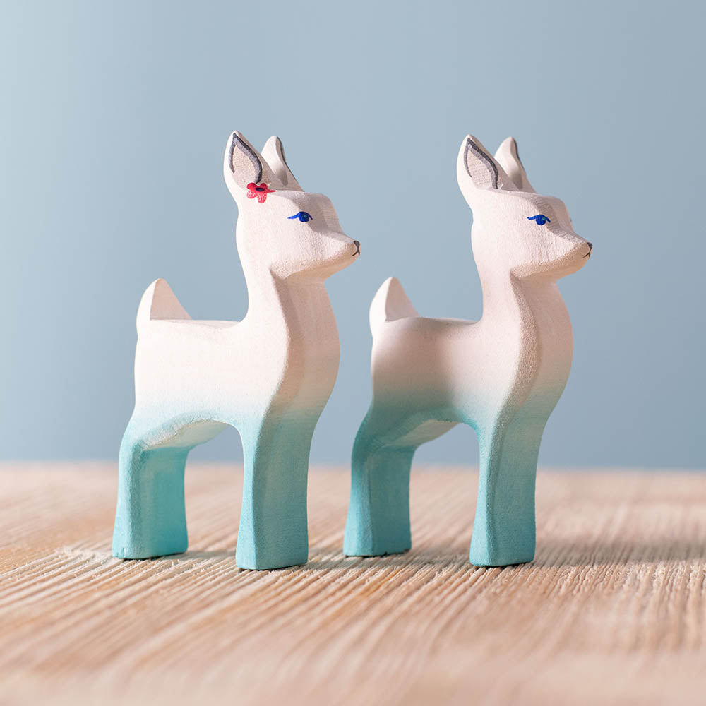 Close up of the Bumbu handmade wooden white fawn and white fawn with flower figures on a wooden surface