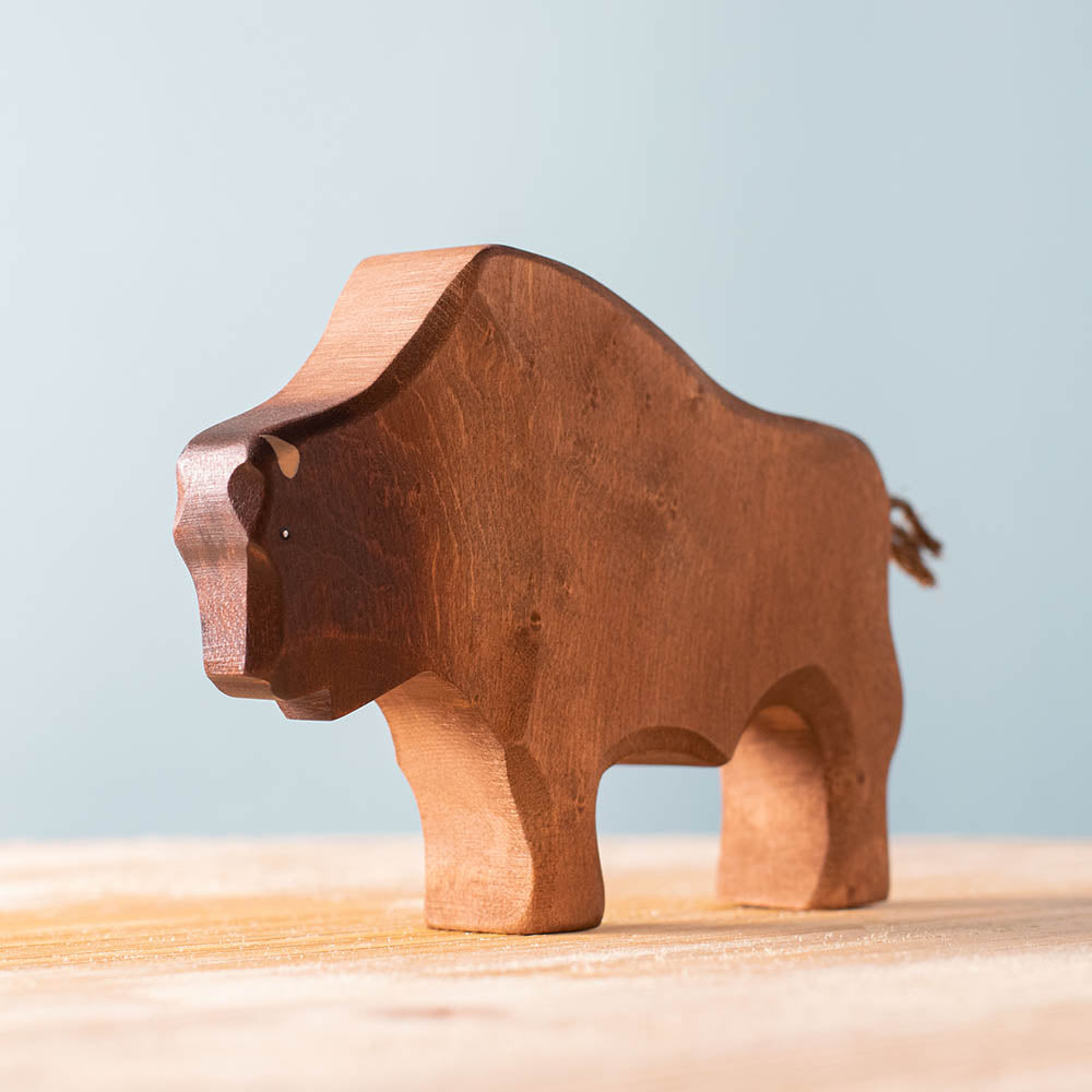 Bumbu handmade natural wooden bison toy figure on a wooden surface in front of a blue background