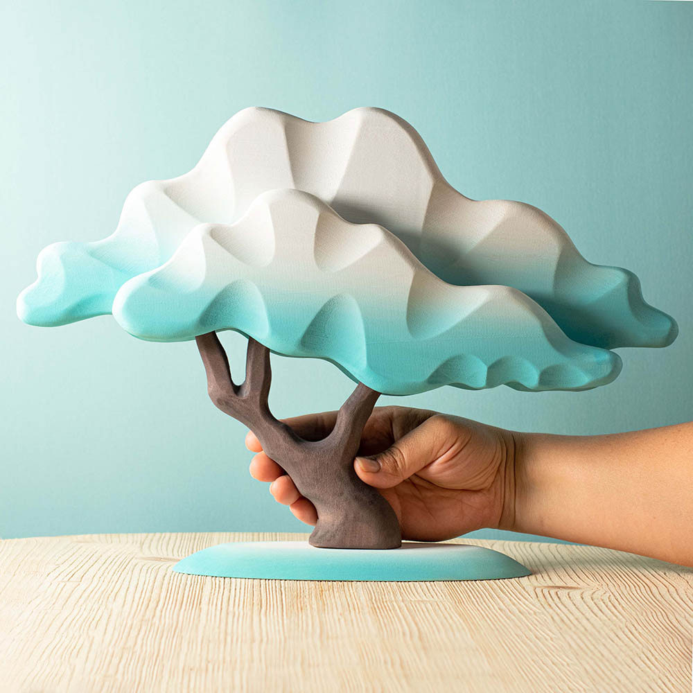 Close up of a hand holding the Bumbu plastic-free blue Japanese winter maple tree toy on a wooden table