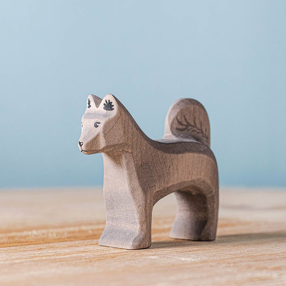 Close up of the Bumbu childrens handmade wooden shurik dog on a wooden table in front of a blue background