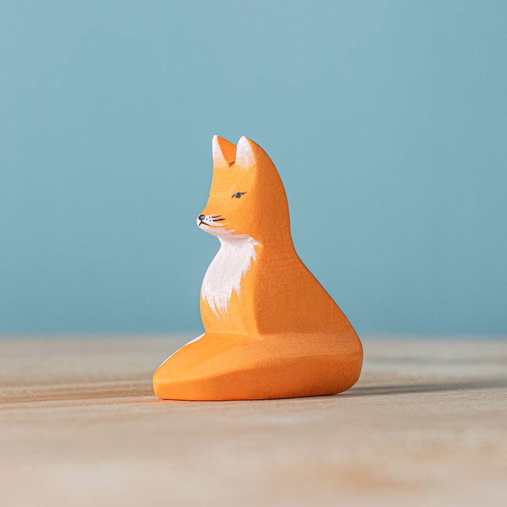 Close up of the childrens Bumbu wooden sitting fox figure on a wooden surface in front of a blue background