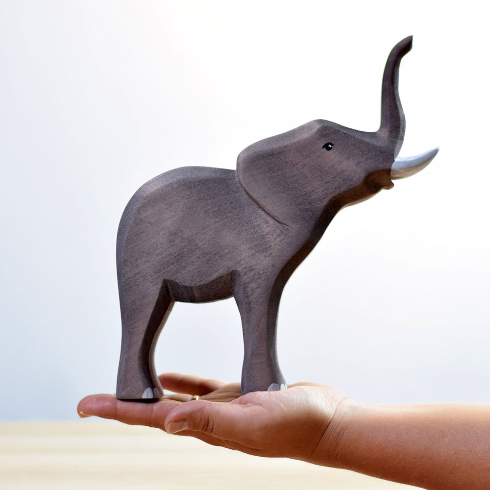 Hand holding the Bumbu eco-friendly large wooden elephant animal figure in front of a white background