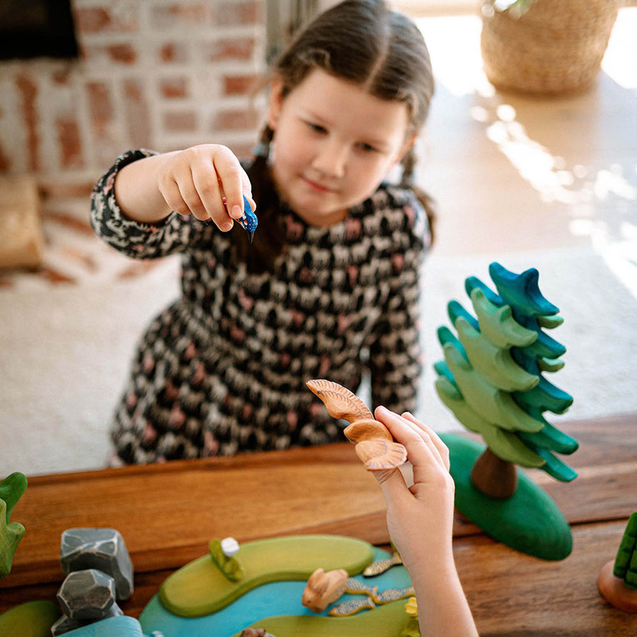 Close up of young children holding up the Bumbu kingfisher and eagle toys above a wooden waterfall scene