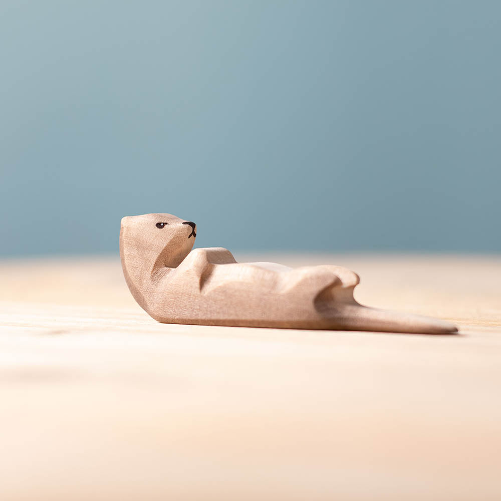 Close up of the Bumbu hand carved sleeping wooden otter toy on a wooden surface in front of a blue background