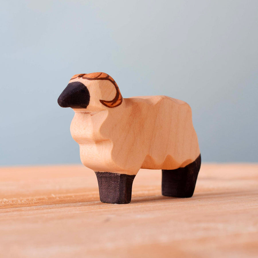 Bumbu handmade wooden standing ram animal figure on a wooden worktop in front of a blue background