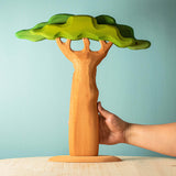 Close up of a hand holding the Bumbu tall trunk baobab tree toy in front of a blue background